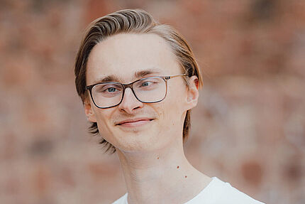 Porträt eines jungen Mannes mit Brille. Er trägt ein weißes Shirt mit dem Logo des Jungen ADFC und schaut in die Kamera.